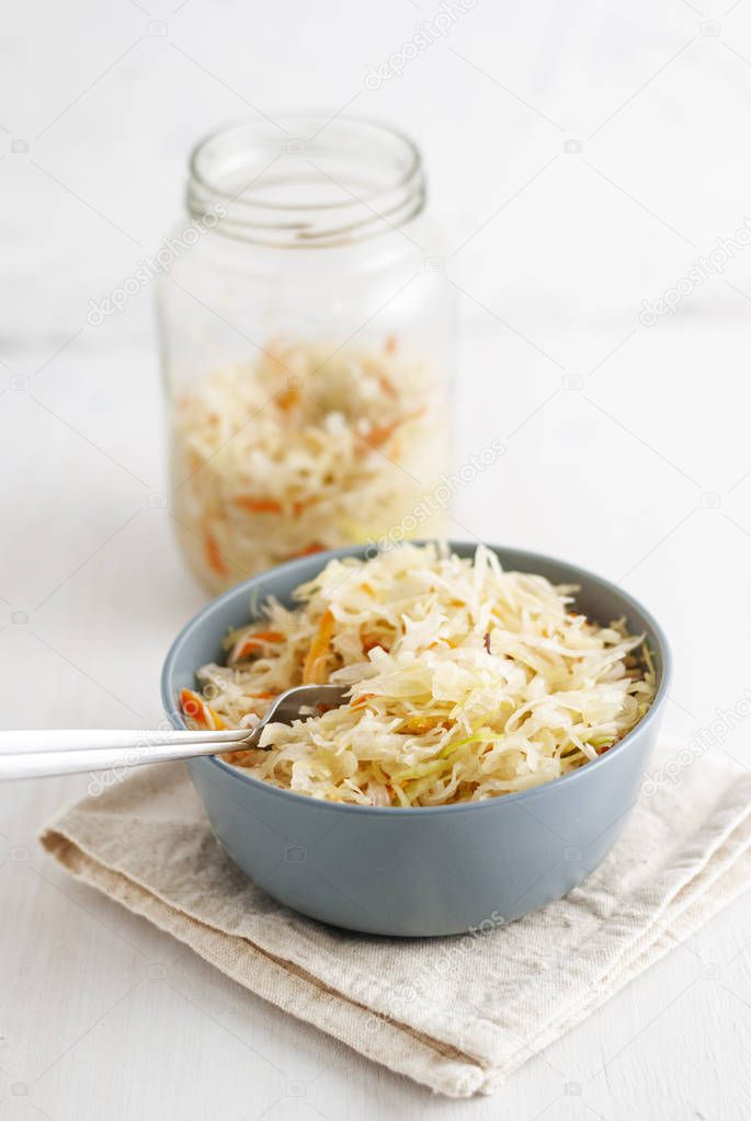 Glass jar and ceramic bowl with delicious fermented cabbage standing on white background