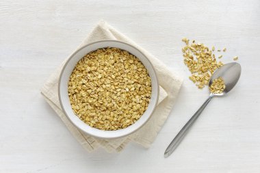 Beyaz seramik tabak beyaz havlu peçete ve metal kaşık ile yukarıdan görüntülenen ve küçük yığın masa yüzeyi üzerinde oturan kuru yulaf ezmesi,