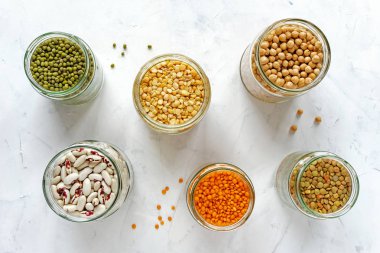 Sağlıklı bir diyet ve beslenme kavramı içinde beyaz bir arka plan üzerinde çeşitli kuru baklagiller mung fasulye, fasulye, mercimek ve bezelye ile dolu açık cam kavanozlar