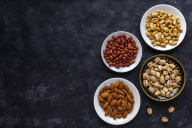 Kopya alanı ile karanlık bir arka plan üzerinde çeşitli taze fındık fıstık, badem ve fıstık ile kâse ile sınır