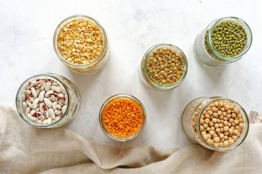 Çeşitli kuru baklagiller ve bakliyat yukarıdan izlendi bezelye, mercimek, fasulye, nohut, beyaz kumaş üzerine cam mutfak kavanoz