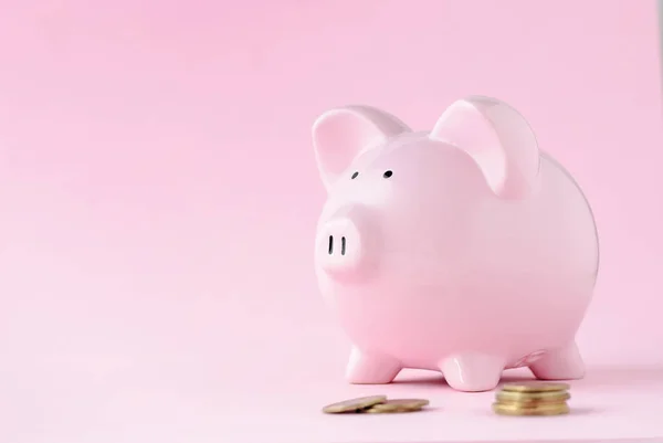 Pink ceramic piggy bank over matching pink background with copy space and loose coins in a banking, savings, investment and finance concept