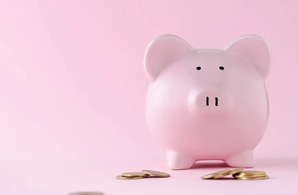 Pink ceramic piggy bank over matching pink background with copy space and loose coins in a banking, savings, investment and finance concept