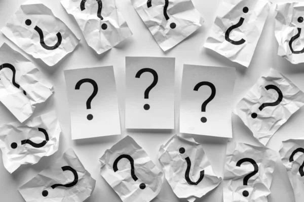 Three question marks on white cards surrounded by a frame of crumpled sheets of paper also printed with question marks in a full frame background concept