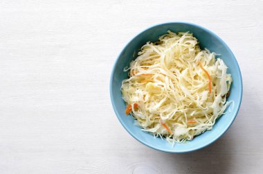 Seramik mavi kase fermente doğranmış çiğ lahana ve havuç, beyaz arka plan üzerinde kopya alanı ile yukarıdan izlendi. Sağlıklı beslenme kavramı