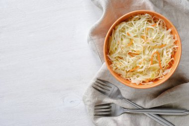 İki çatal ve doğranmış çiğ lahana ile havuç, portakal kase hizmet katlanmış gri havluda. Beyaz arka plan üzerinde yukarıdan izlendi