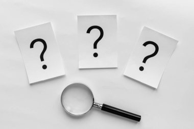 Bir çizgi üstü bir büyüteç kavramsal bir görüntüde beyaz bir arka plan üzerinde beyaz kartlarda üç soru işaretleri basılır