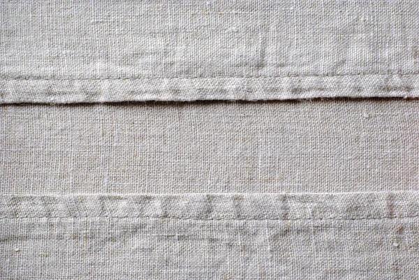 Stitched seams or edges on natural linen textile arranged as two borders to the sides over woven fabric centre with copy space