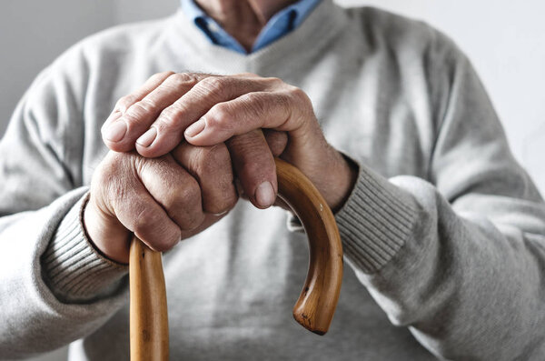 Hands of an elderly man resting on a walking cane