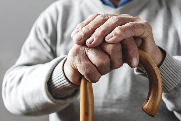 Hands of an elderly man resting on a walking cane