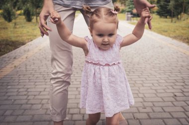 Genç anne kızına yürümeyi öğretiyor.