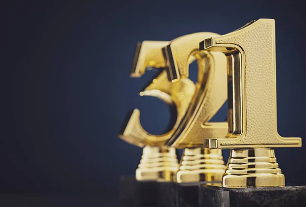 Three golden number trophies in front of blue — Stock Photo, Image