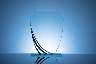 Elegant blank glass shield trophy on dark blue background ready to be engraved for the winner of a competition or race clipart