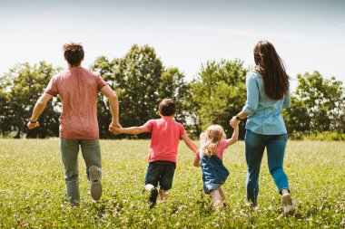 Kaygısız genç bir aile, ilkbaharda ya da yaz aylarında, sağlıklı bir açık hava yaşam tarzı konseptiyle el ele kameradan kaçıyor.