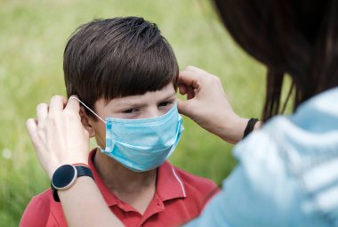 Anne, Covid-19 ya da Coronavirus salgını sırasında yeşil çimenlere karşı korunmak için maske takan genç bir çocuğu yakından görüyor.