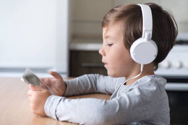 Kulaklıklı ve tabletli bir çocuk mutfaktaki masada oturuyor..