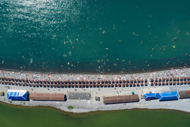 Sahilde kum üzerinde üst hava görünümünü tükürmek. Satır şemsiye ve şezlong, sıcak mavi deniz ve tatil vericiler eğleniyor. Kopya alanı