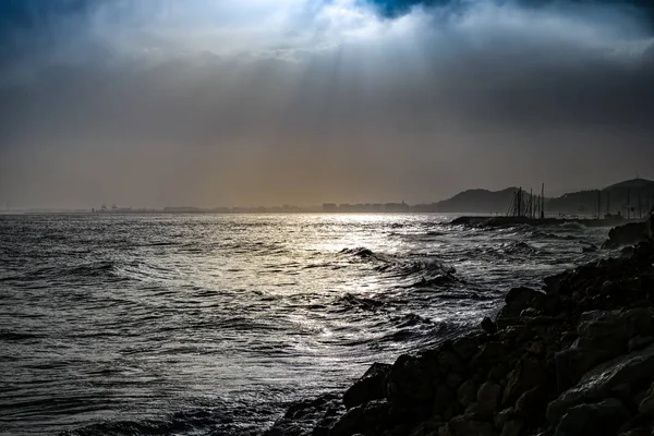 Драматические солнечные лучи сквозь облачное темное небо над морем — стоковое фото