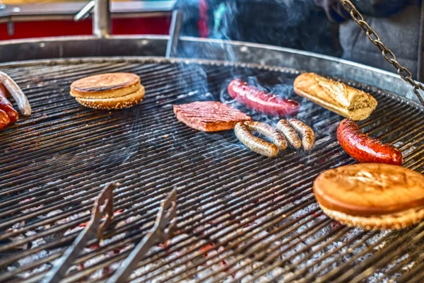 Hamburger und Würstchen auf dem Grill mit Rauch — Stockfoto