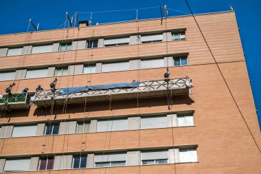 workers on the exterior scaffold elevator to repair the building
