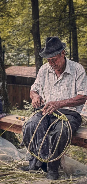 Un vieil homme roumain tisse des paniers en osier — Photo