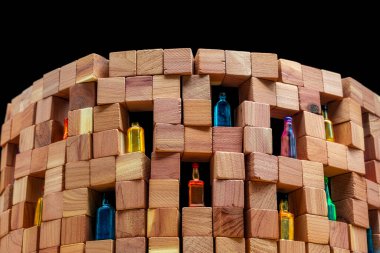 A wall made of wooden cubes with various miniature bottles of alcohol without labels on dark bacground