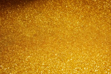Altın, parıltılı bir yüzeye yakın çekim. Doku yoğun bir şekilde ışığı yansıtan küçük, parıldayan parçacıklarla doludur..