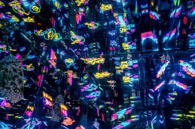 Neon ışıklı, yoğun bir şehir gece hayatı sahnesi. Sahne çeşitli tabelalarla, barlarla, kulüplerle ve dükkanlarla dolu. Atmosfer hareketli bir şehir gece hayatının özünü yakalıyor.