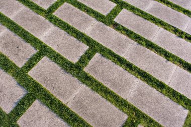Alternatif açık gri beton levhalar ve dar yeşil çimen şeritleri içeren dikdörtgen bir kaldırım deseni..
