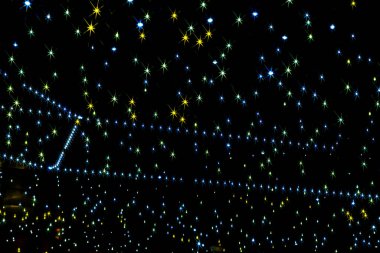 Siyah arkaplanı olan yıldızlı bir gökyüzü. Her yıldızın merkezden yayılan birden fazla ince ve renkli ışınları olan parlak bir yıldız patlaması deseni vardır..