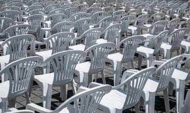 Photograph of an outdoor seating arrangement featuring numerous white plastic chairs and tables arranged in rows on a sunlit, cobblestone pavement