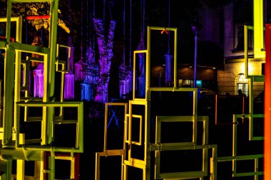 an abstract art installation featuring numerous rectangular frames of varying sizes, stacked and overlapping. The frames are illuminated by neon lights, creating a vibrant, futuristic atmosphere.