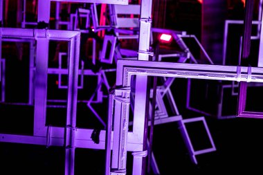 an abstract art installation featuring numerous rectangular frames of varying sizes, stacked and overlapping. The frames are illuminated by neon lights, creating a vibrant, futuristic atmosphere.