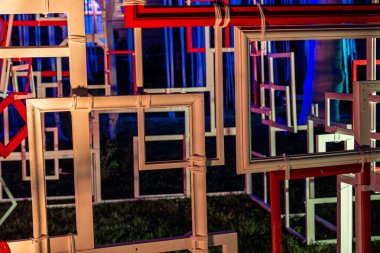 an abstract art installation featuring numerous rectangular frames of varying sizes, stacked and overlapping. The frames are illuminated by neon lights, creating a vibrant, futuristic atmosphere.