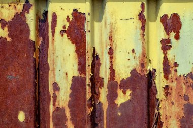 rusted, weathered yellow-painted metal panels. The panels show extensive peeling and flaking, revealing underlying rusty red and brown layers.