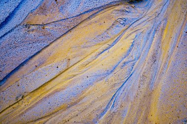 textured multicolored sand surface at abandoned kaolin mine, the patterns resemble streaks of natural sediment layers, creating a dynamic, abstract visual effect.