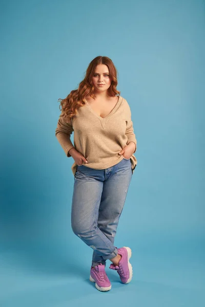 Menina gorda confiante em jeans e camisola posando no estúdio — Fotografia de Stock