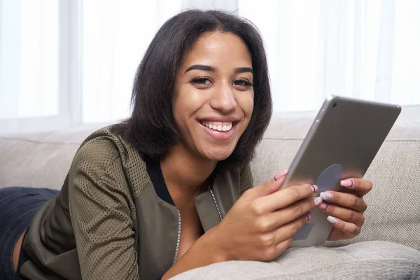 Glückliches Teenager-Mädchen mit digitalem Tablet auf dem Sofa lizenzfreie Stockfotos