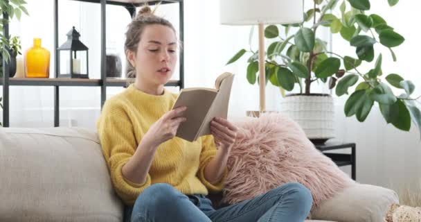 Kvinna läser en bok om soffan hemma — Stockvideo