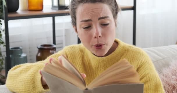 Mujer leyendo un libro en el sofá en casa — Vídeos de Stock