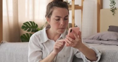 Evde cep telefonu kullanan şok olmuş bir kadın.