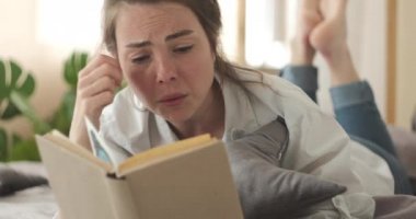 Evde kitap okurken ağlayan üzgün kadın.