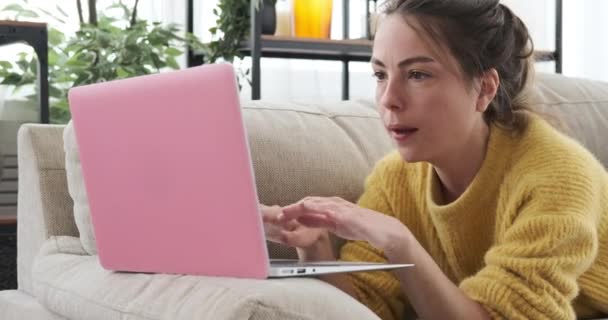 Γυναίκα που χρησιμοποιεί φορητό υπολογιστή που βρίσκεται στον καναπέ στο σπίτι — Αρχείο Βίντεο