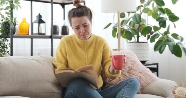 Γυναίκα διαβάζει ένα βιβλίο και πίνει καφέ στον καναπέ στο σπίτι — Αρχείο Βίντεο