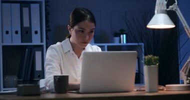 İş kadını gece ofisinde dizüstü bilgisayar kullanıyor ve notlar yazıyor.