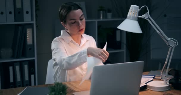 Forretningskvinne bruker bærbar PC og gjør papirarbeid på nattkontoret – stockvideo