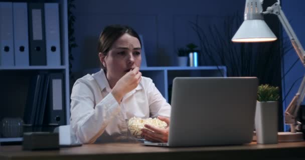 หญิงนักธุรกิจที่เศร้า กินข้าวโพดคั่ว และดูหนังที่ออฟฟิศตอนกลางคืน — วีดีโอสต็อก