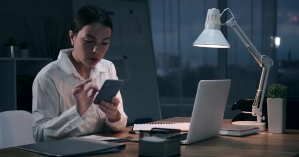 Businesswoman pomocí telefonu a pracuje na notebooku v noční kanceláři — Stock video