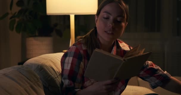 Γυναίκα τρώει ποπ κορν και διαβάζει βιβλίο το βράδυ — Αρχείο Βίντεο