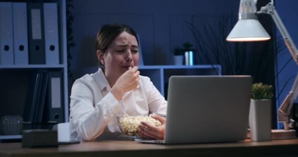 Грустная деловая женщина ест попкорн и смотрит кино в ночном офисе — стоковое видео